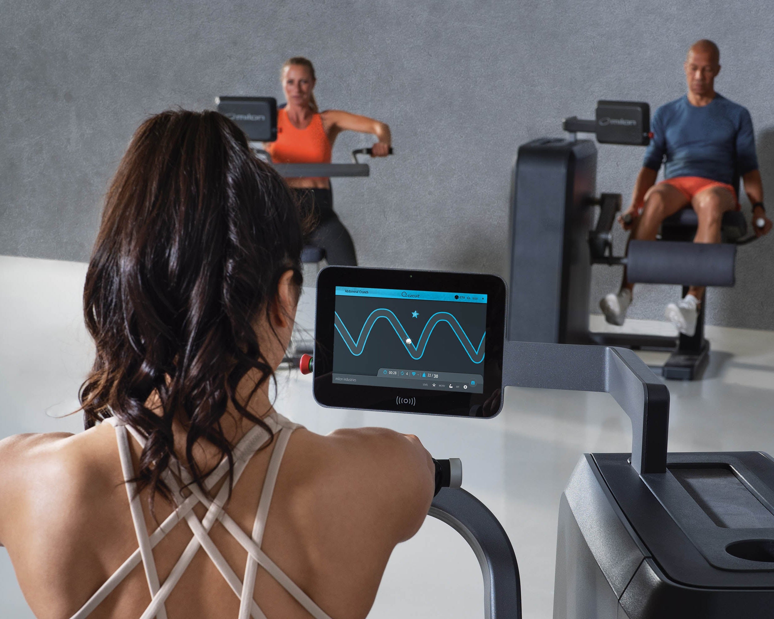 People exercising on fitness equipment with a digital display in the foreground.